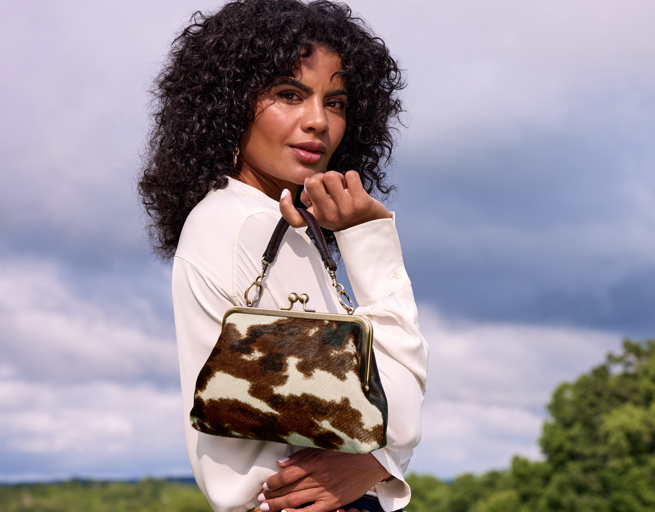 Model holding cow print frame bag by Patricia Nash, vintage-inspired Cavallino leather accessory in lifestyle setting