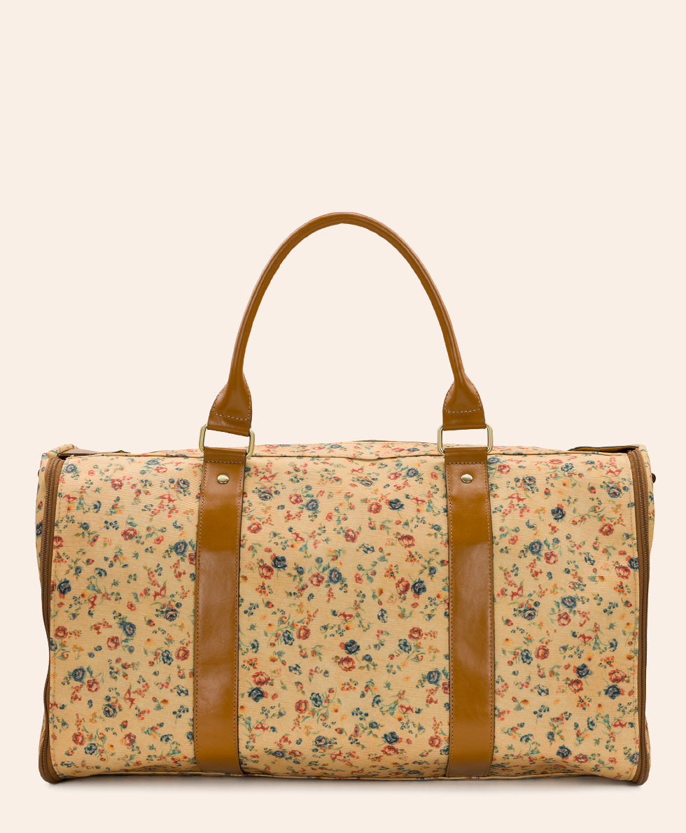 A vintage-style duffel bag with a beige floral print and tan leather handles and trim, shown against a solid cream background.