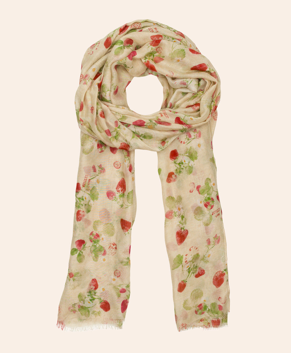 A lightweight cream scarf with a delicate strawberry and leaf print, draped in a loop against a solid pale beige background.