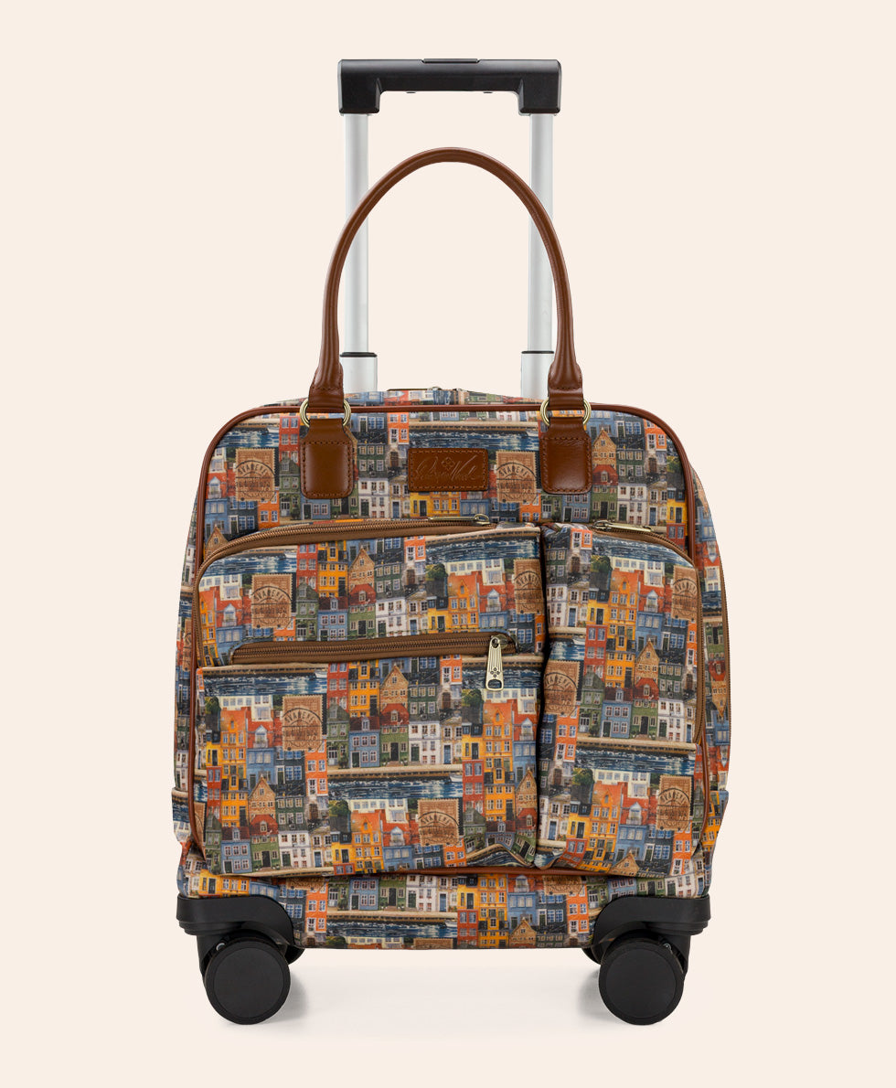 A rolling travel bag with a multicolor cityscape print, brown leather handles, and a telescoping handle, shown against a solid light beige background.
