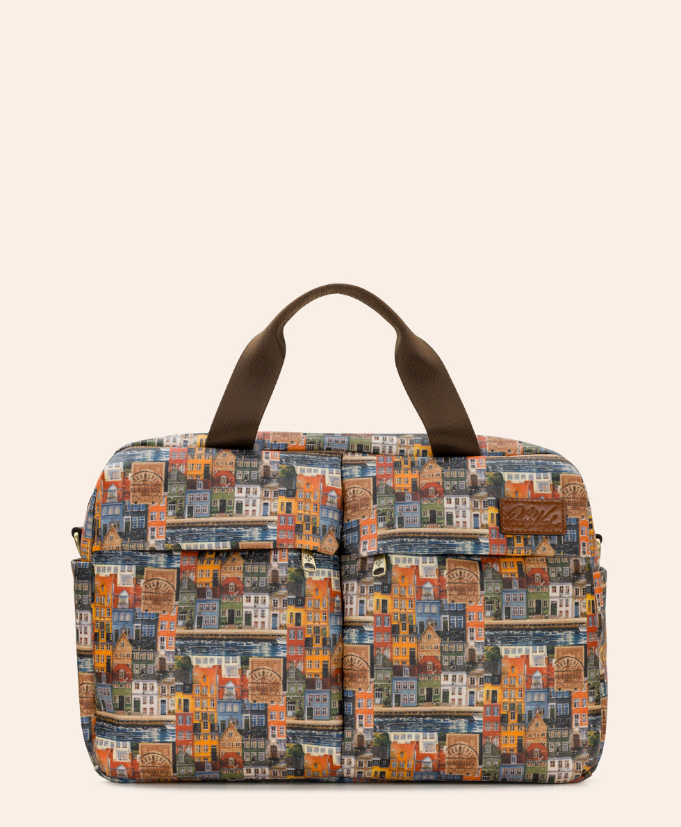 A structured tote bag featuring a colorful, dense illustration of vintage houses and buildings in warm tones, with dark brown top handles and a small brown leather patch on the front.