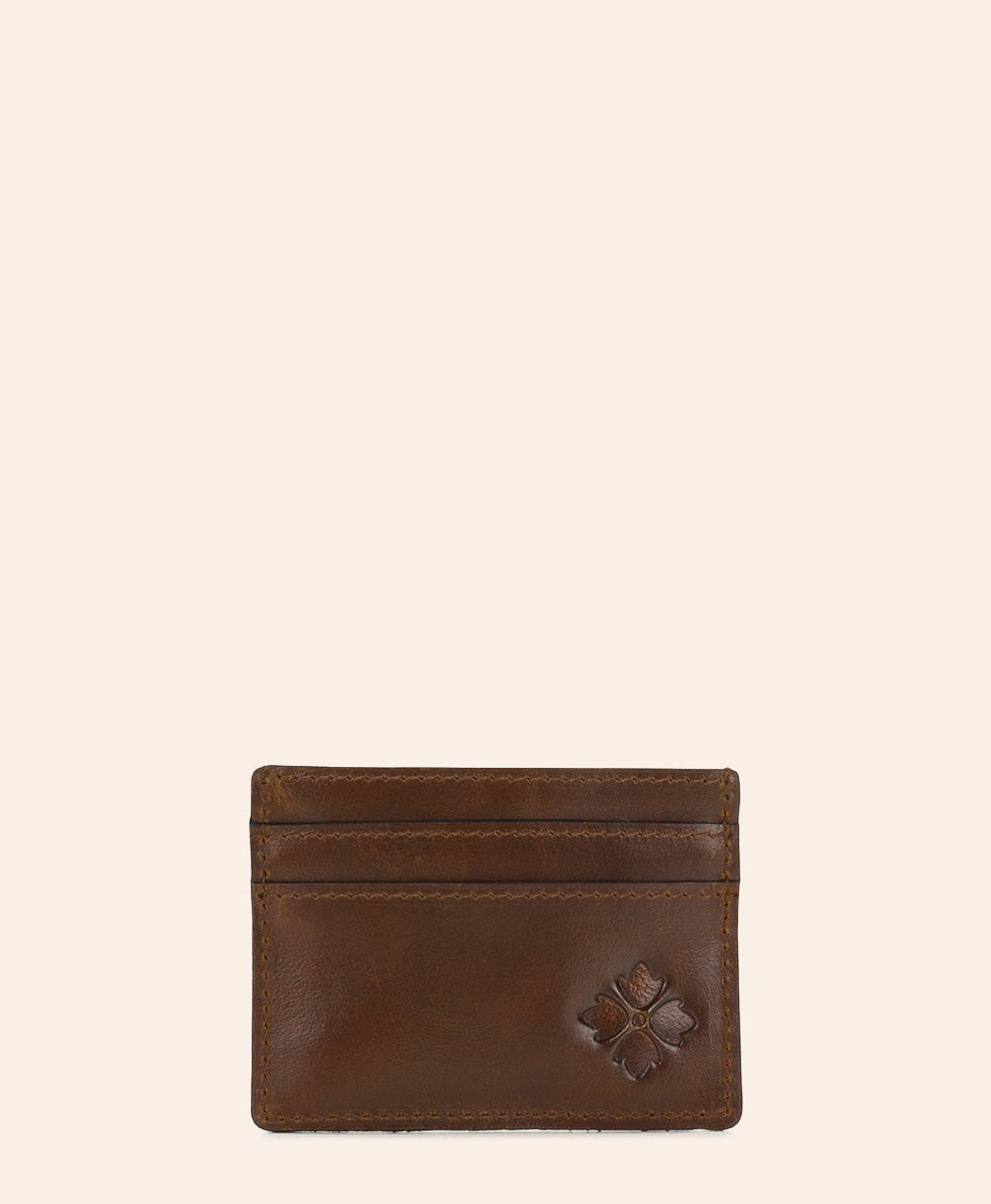 A brown leather card holder wallet with a debossed clover logo on the bottom right, displayed against a solid off-white background.