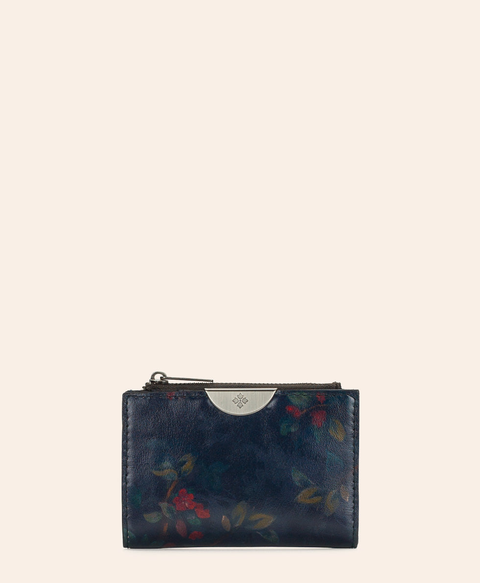 A small zip-around wallet in dark navy blue leather with a subtle floral print in muted red, green, and yellow tones, featuring a silver-tone metal accent at the top.