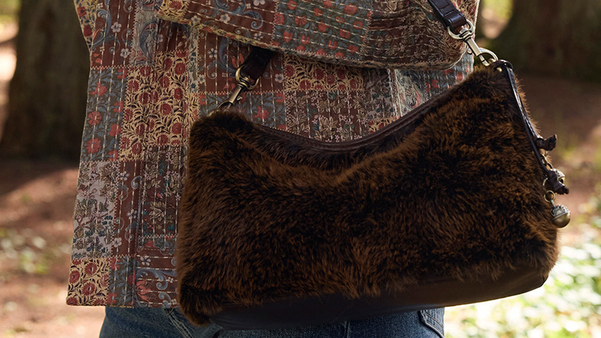 A brown faux-fur shoulder bag with dark trim and a patterned quilted jacket, worn by a person outdoors in a wooded setting.
